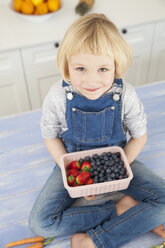 Porträt eines niedlichen Mädchens, das ein Körbchen mit Blaubeeren und Erdbeeren auf dem Küchentisch hält - CUF05765