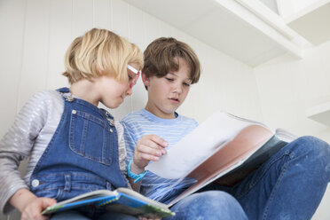Mädchen liest mit Bruder auf dem Küchentisch ein Bilderbuch - CUF05768