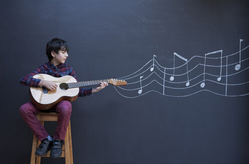 Gitarre spielender Junge vor einer Kreidetafel mit Notenschrift an der Wand - CUF05802