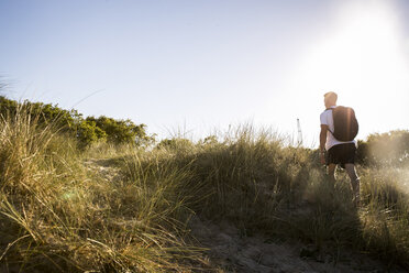 Rear view of young man hiking across sand dunes - CUF05880