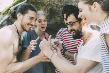 Fünf erwachsene Freunde beim Bouldern, die lachend auf ihr Smartphone schauen, Lombardei, Italien - CUF05897