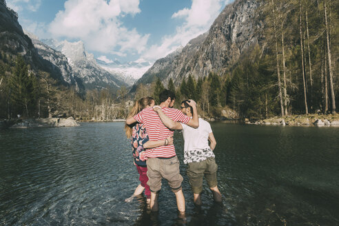 Rückansicht von drei jungen erwachsenen Freunden, die knöcheltief in einem Bergsee stehen, Lombardei, Italien - CUF05898