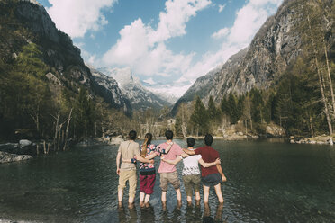 Rear view of five adult friends ankle deep in mountain lake, Lombardy, Italy - CUF05899