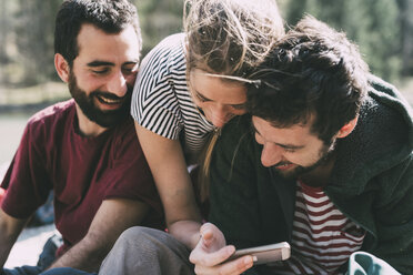 Drei junge erwachsene Freunde schauen und lachen über ein Smartphone, Lombardei, Italien - CUF05903