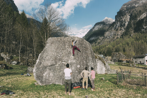 Rückansicht von erwachsenen Boulderern, die einer jungen Frau beim Klettern zusehen, Lombardei, Italien, lizenzfreies Stockfoto