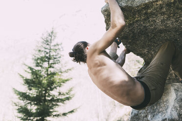 Bare chested male boulderer climbing boulder, Lombardy, Italy - CUF05916