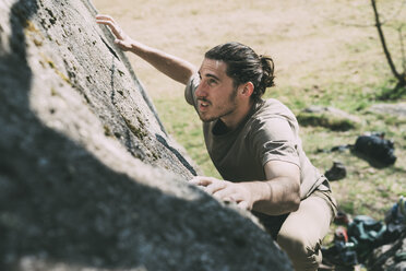 Young male boulderer climbing up boulder, Lombardy, Italy - CUF05920