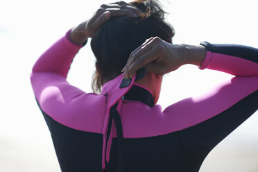 Rear head and shoulder view of mature female paddleboarder fastening wetsuit - CUF05950