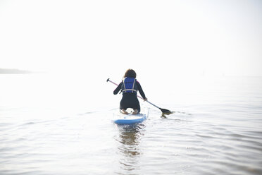 Rückansicht eines weiblichen Paddelboardfahrers, der auf dem nebligen Meer paddelt - CUF05951