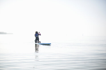 Rückansicht eines weiblichen Paddelboardfahrers, der auf dem nebligen Meer paddelt - CUF05952