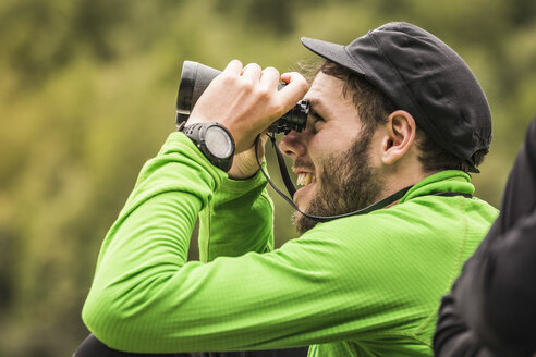 Young male backpacker looking through binoculars in Queulat National Park, Chile - CUF05954