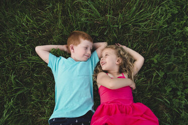 Overhead-Porträt eines Jungen und einer Schwester, die im Gras liegen und sich gegenseitig anschauen - CUF05968