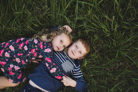 Overhead-Porträt eines Jungen und einer Schwester, die im Gras liegen und sich umarmen, lizenzfreies Stockfoto