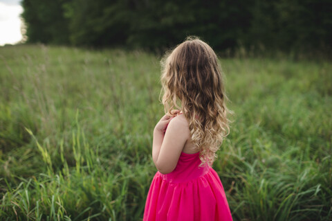 Rückansicht eines blondhaarigen Mädchens mit Blick auf ein Feld, lizenzfreies Stockfoto