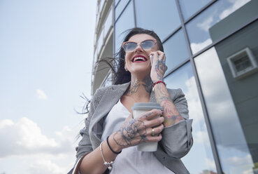 Geschäftsfrau, die im Freien spazieren geht, Kaffee in der Hand, Smartphone benutzt, Tätowierungen an den Händen, niedriger Blickwinkel - CUF05979