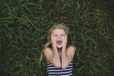 Overhead-Porträt eines im Gras liegenden Mädchens mit den Händen auf ihren Wangen - CUF05983