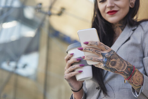 Geschäftsfrau im Freien, hält Kaffeetasse, benutzt Smartphone, Tätowierungen an den Händen, Mittelteil - CUF05985
