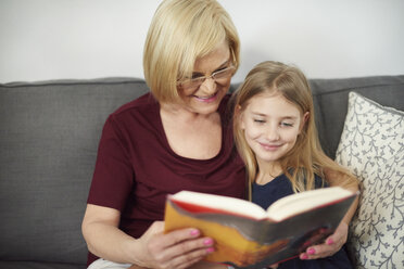 Grandmother and granddaughter reading book on sofa - CUF06002