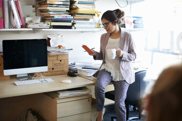 Woman sitting on desk looking at notepad - CUF06120