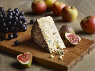 Still life of Stilton on chopping board with figs, apples and grapes - CUF06232