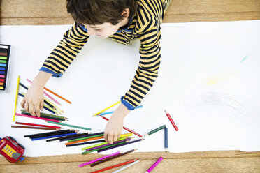 Overhead view of boy lying on floor drawing on long paper - CUF06358