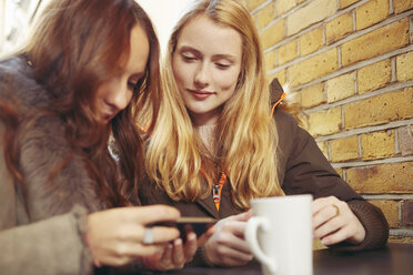 Zwei Freundinnen, die im Freien sitzen, Kaffee trinken und auf ihr Smartphone schauen - CUF06363