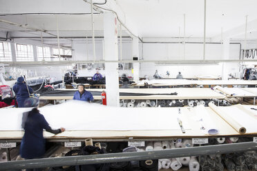 Female factory workers unrolling textiles in clothing factory - CUF06378