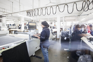 Weibliche Fabrikarbeiterin bei der Bedienung einer Fertigungsmaschine in einer Bekleidungsfabrik - CUF06380