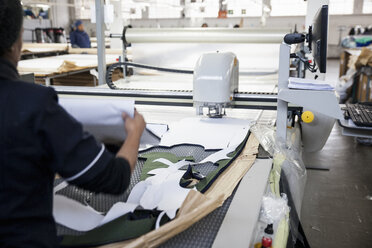 Rückansicht eines Fabrikarbeiters, der ein zugeschnittenes Textilmuster von einer Musterschneidemaschine in einer Bekleidungsfabrik entfernt - CUF06387