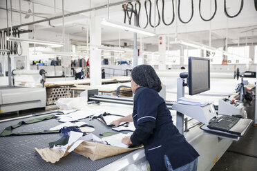 Fabrikarbeiter, der geschnittene Textilmuster von der Schnittmusterschneidemaschine in einer Bekleidungsfabrik entfernt - CUF06388