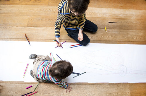 Draufsicht auf ein männliches Kleinkind und einen großen Bruder, die auf dem Boden sitzen und auf einem langen Papier zeichnen - CUF06392