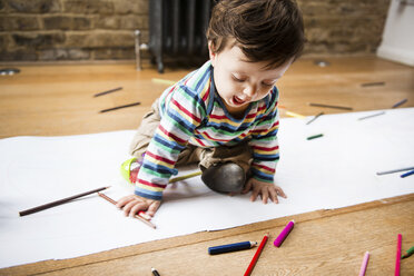 Männliches Kleinkind sitzt auf dem Boden und zeichnet auf einem langen Papier - CUF06393