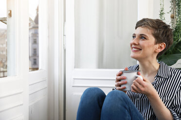 Happy woman sitting relaxed at window, drinking coffee - FKF02888