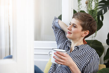 Happy woman sitting relaxed at window, drinking coffee - FKF02889