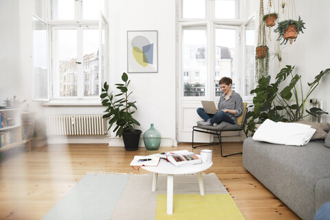 Frau sitzt auf einem Stuhl zu Hause und benutzt einen Laptop, lizenzfreies Stockfoto