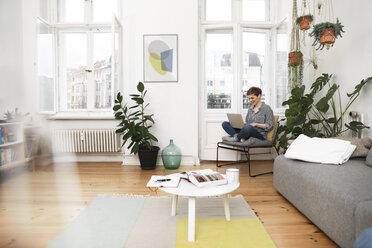 Woman sitting in chair at home, using laptop - FKF02890