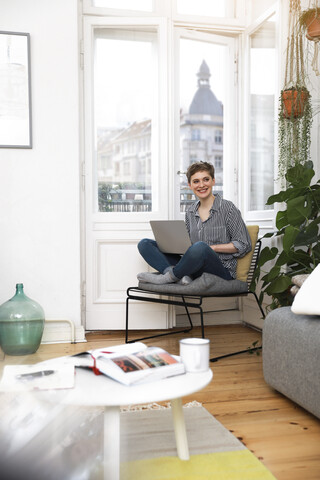 Woman sitting in chair at home, using laptop stock photo