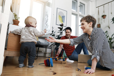 Happy family sitting on ground, playinhg with their little daughter - FKF02899