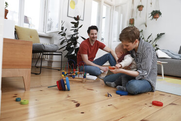 Glückliche Familie sitzt auf dem Boden und spielt mit ihrer kleinen Tochter - FKF02900