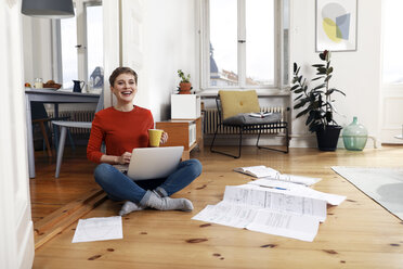 Woman sitting cross-legged on floor of her home, using laptop - FKF02904