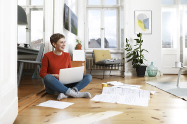 Woman sitting cross-legged on floor of her home, using laptop - FKF02906