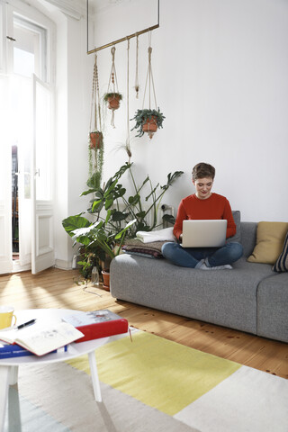 Frau sitzt auf der Couch und benutzt einen Laptop, lizenzfreies Stockfoto