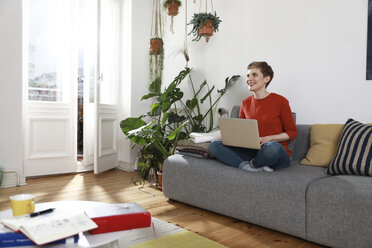 Frau sitzt auf der Couch und benutzt einen Laptop - FKF02913