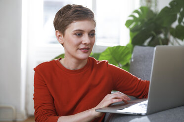 Woman sitting at home, using laptop - FKF02914