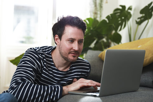 Mann sitzt zu Hause und benutzt einen Laptop - FKF02915