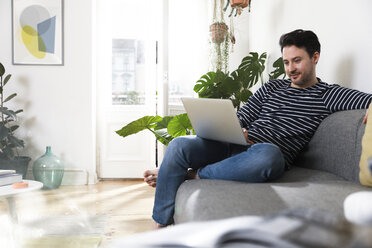 Mann sitzt zu Hause und benutzt einen Laptop - FKF02923