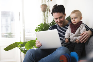 vater sitzt mit seiner kleinen Tochter auf der Couch und benutzt einen Laptop - FKF02925