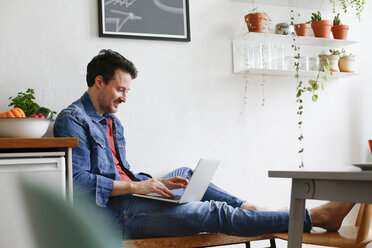 Man sitting at home, using laptop - FKF02940