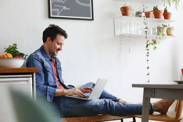 Mann sitzt zu Hause und benutzt einen Laptop - FKF02940