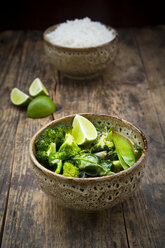 Green thai curry with broccoli, pak choi, snow peas, baby spinach, lime and bowl of rice in the background - LVF06976